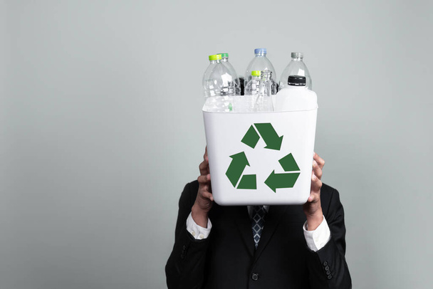ビジネスマンは、隔離された背景にプラスチックボトルで満たされたごみ箱を保持します。緑の環境とコミュニティのための企業責任。廃棄物分離と管理の概念。Alter - 写真・画像
