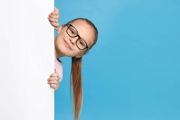 Cute girl looking out of placard against light blue background. Space for text - Fotografie, Obrázek