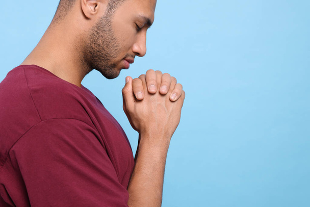 African American man with clasped hands praying to God on light blue background, closeup. Space for text - Foto, imagen