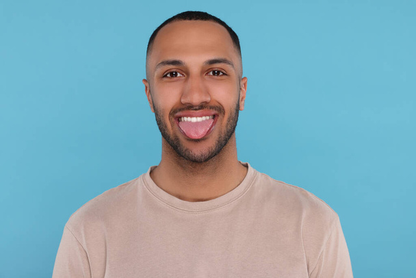 Happy young man showing his tongue on light blue background - Φωτογραφία, εικόνα