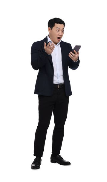 Shocked businessman in suit with smartphone on white background - Valokuva, kuva