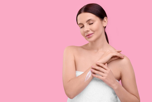 Beautiful woman with smear of body cream on her arm against pink background, space for text - Photo, image