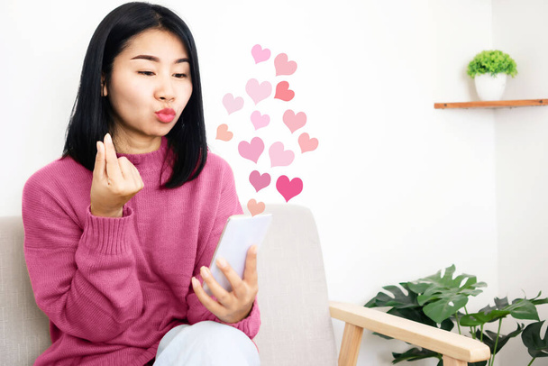 Mujer asiática usando teléfono móvil citas en línea haciendo señal de mano mini corazón coqueteando con su amante de distancia - Foto, imagen