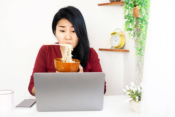 workaholic mujer de negocios asiática ocupada y sobrecargada de trabajo en el portátil y comer fideos en el escritorio de la oficina en casa - Foto, imagen