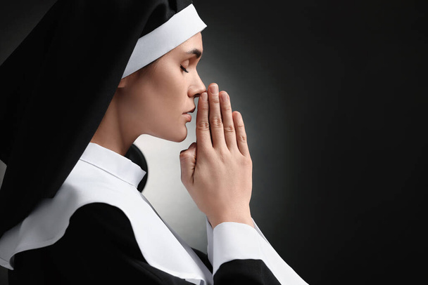 Nun with clasped hands praying to God on black background. Space for text - Fotografie, Obrázek