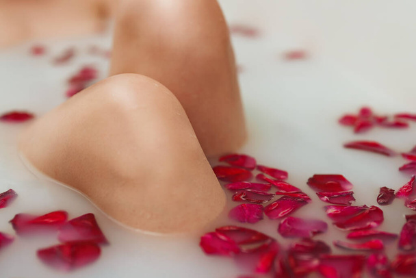 Vrouwenknieën. Vrouw ligt in een bad met melk en rozenblaadjes. - Foto, afbeelding