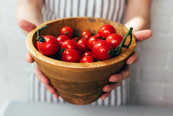 As mãos femininas mantêm tomates cereja em uma chapa profunda de madeira close-up à luz do dia. Vista frontal - Foto, Imagem