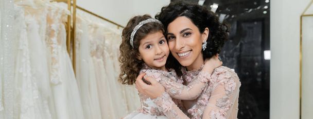 brunette Lähi-idän nainen aaltoileva hiukset upea hääpuku halaus söpö tytär söpö kukka pukea morsiussalonki, ostokset, onnellisuus, erityinen hetki, yhdessä, banneri - Valokuva, kuva