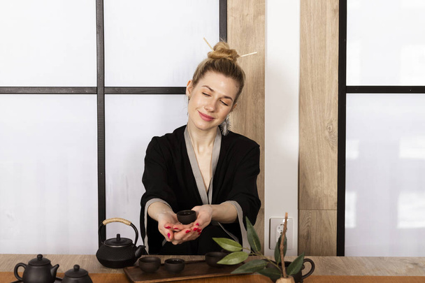 Attraktives weißes Mädchen in Kimono und Haarsträhnen trinkt Tee im japanischen Stil. Japanische Teezeremonie. - Foto, Bild