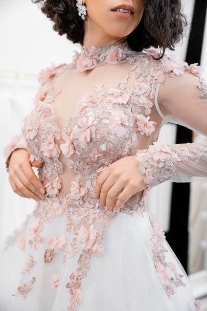 Ausgeschnittene Ansicht einer brünetten Frau, die in einem wunderschönen und floralen Hochzeitskleid in einem luxuriösen Salon um weiße Tüll-Stoffe steht, Brautshopping, zukünftige Braut, Details  - Foto, Bild