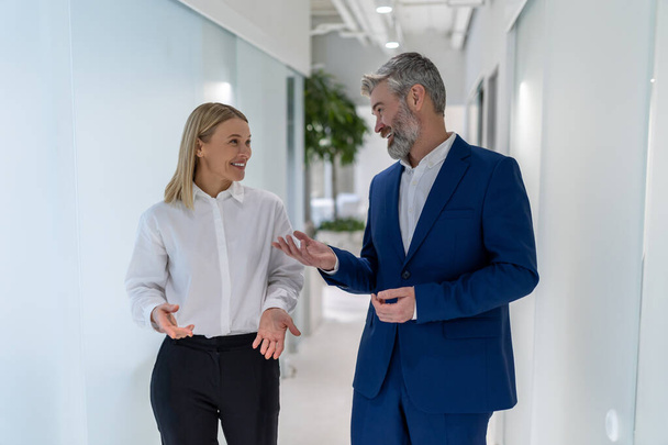 Pleased elegant businessman communicating with his female colleague in the office corridor - Foto, Imagem