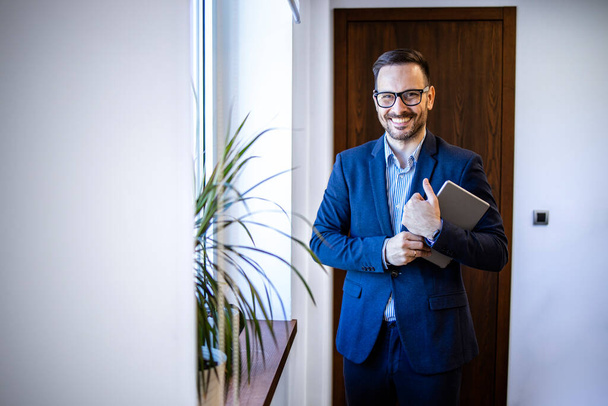 Портрет улыбающегося и ответственного бизнесмена, стоящего в офисе компании. - Фото, изображение