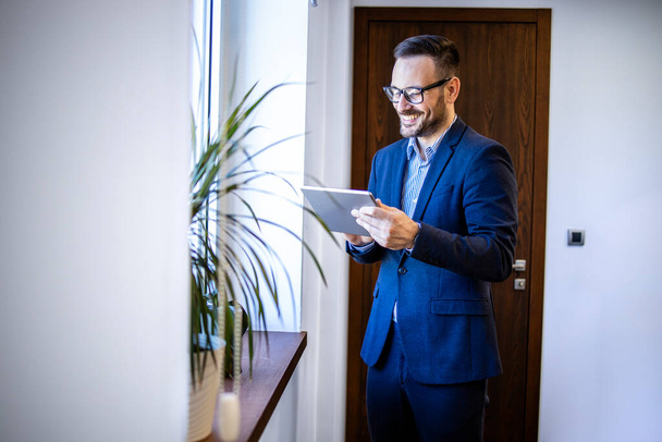 Веселий менеджер у діловому костюмі стоїть в офісі за допомогою цифрового планшетного комп'ютера
. - Фото, зображення