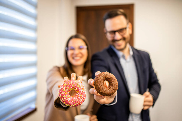 Colleagues at work showing delicious donuts at coffee break. - Foto, afbeelding