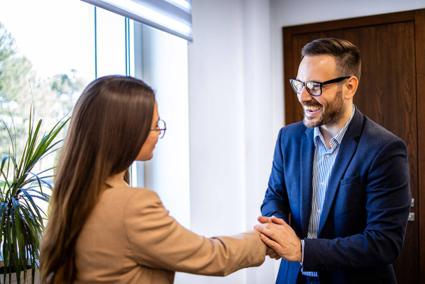 Man in business pak schudden handen en verwelkomen nieuwe vrouwelijke collega in het kantoor. - Foto, afbeelding