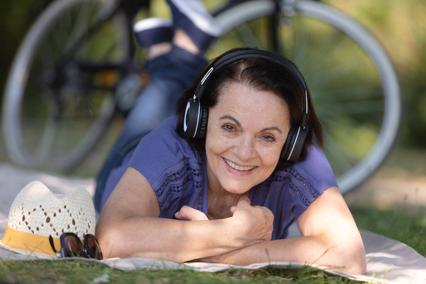 mature woman listening to music while laying on the grass - Фото, изображение
