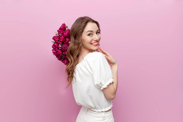 young attractive woman in white festive clothes holding bouquet of pink tulips on pink isolated background, girl with flowers, the concept of spring and women's holiday - Foto, Imagem