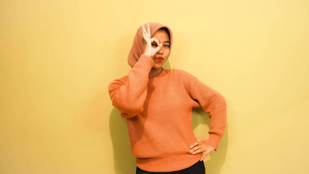 young asian woman using finger pointing in different directions with blank copy space standing over isolated orange background. Pointing finger. Giving directions - Foto, imagen