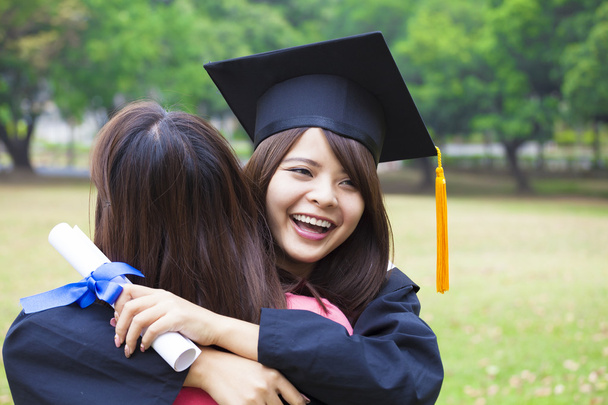 jonge vrouwelijke afgestudeerde haar vriend knuffelen tijdens graduatie ceremonie - Foto, afbeelding