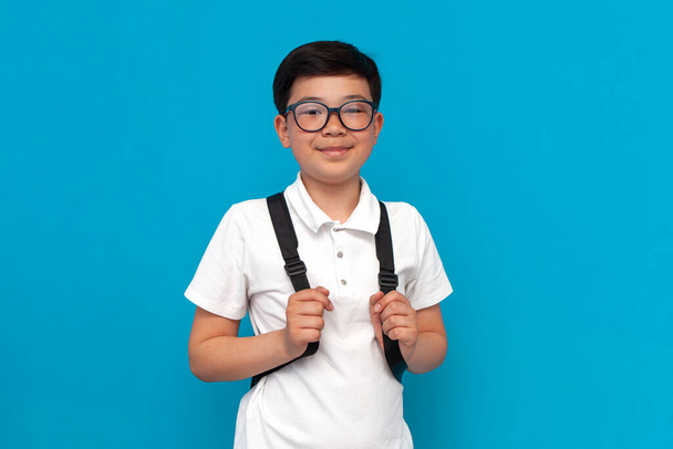 little asian schoolboy in glasses with backpack smiles on blue background, korean child goes back to school to study - Fotoğraf, Görsel
