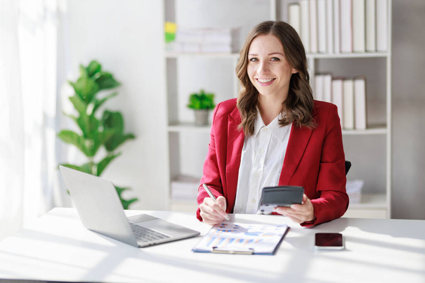Concept of business office woman working,Businesswoman smile while working about her invesment plan with analyzing document and business investment graph data by using laptop on desk in workstation. - Zdjęcie, obraz
