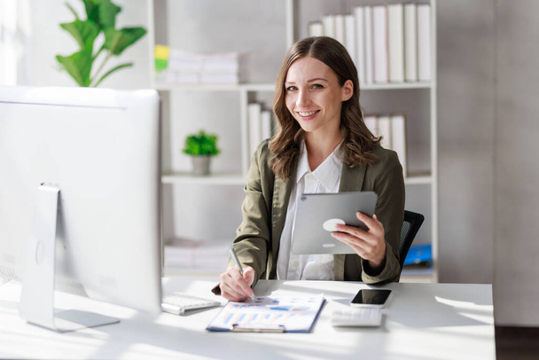 Concept of business office woman working,Businesswoman smile while working about her invesment plan with analyzing document and business investment graph data by using laptop on desk in workstation. - Фото, зображення