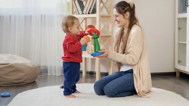 Симпатичный годовалый мальчик играет с мамой и собирает игрушечную башню. Развитие ребенка, детские игры, образование и обучение - Фото, изображение