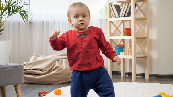 1歳の男の子が立ち上がり、リビングルームでカーペットの上で最初の一歩を踏み出す - 写真・画像