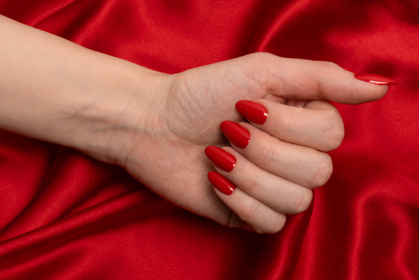 Beautiful red manicure on woman hands on a luxury red silk backround.  - Foto, immagini