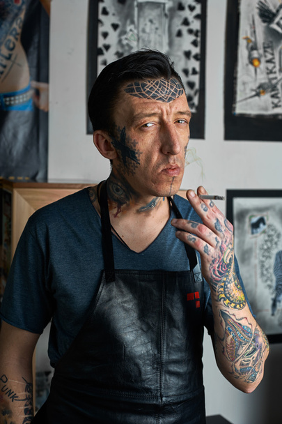 Tattooed man in apron smoking a cigarette - 写真・画像
