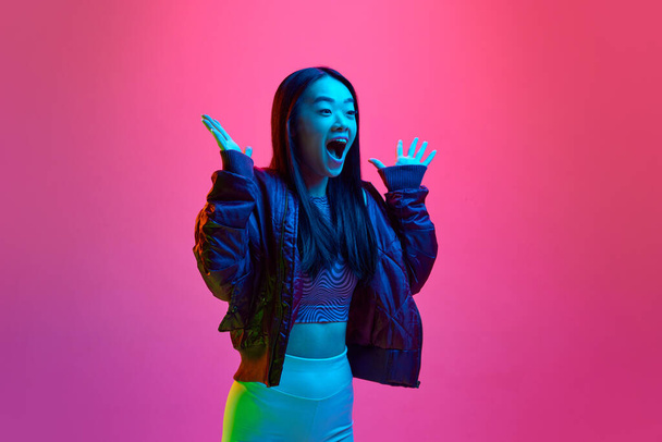 Portrait of young korean girl posing with positive shock expression against pink studio background in neon light. Surprise. Concept of emotions, facial expression, youth, lifestyle, inspiration, ad - Фото, изображение