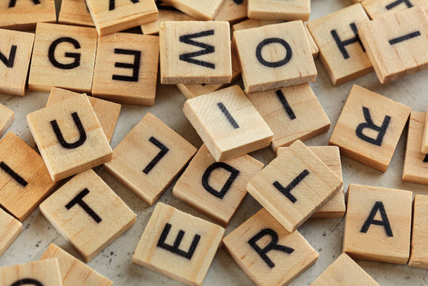 Pile of wooden tiles with various letters scattered on white stone like board, closeup view from above - Foto, afbeelding