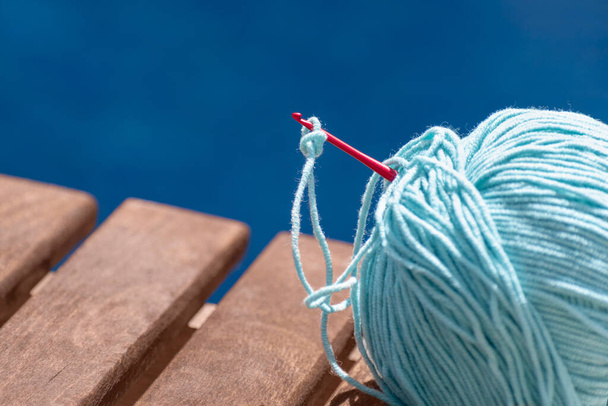 Ball of yarn for crochet on wooden bench isolated on blue swimming pool area background. Hobby, relaxation, needlework, knitting, handicraft, free time on summer vacation - Photo, Image