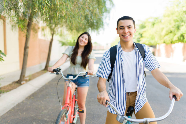 Όμορφος άντρας και όμορφη γυναίκα χαμογελώντας φορώντας σακίδια φαίνονται ευτυχισμένοι ενώ οδηγούν τα ποδήλατά τους έξω το καλοκαίρι - Φωτογραφία, εικόνα