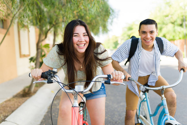 Привлекательная пара смотрит друг другу в глаза, улыбаясь и смеясь, веселясь во время свидания на открытом воздухе, катаясь на велосипеде - Фото, изображение