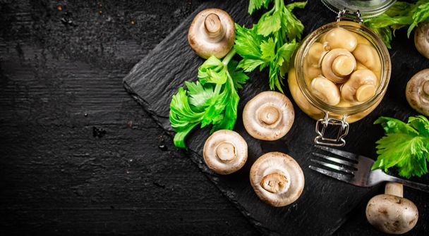 Pickled mushrooms in a jar with greens on a stone board. On a black background. High quality photo - Foto, Imagem