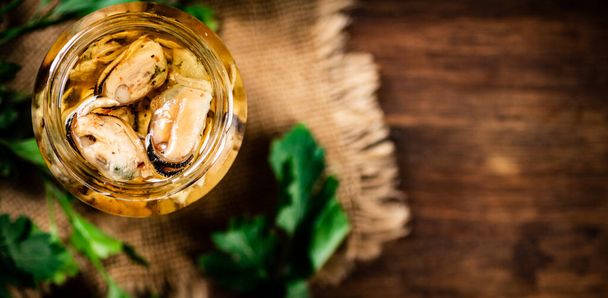 Open glass jar with pickled mussels with parsley. On a wooden background. High quality photo - Фото, изображение