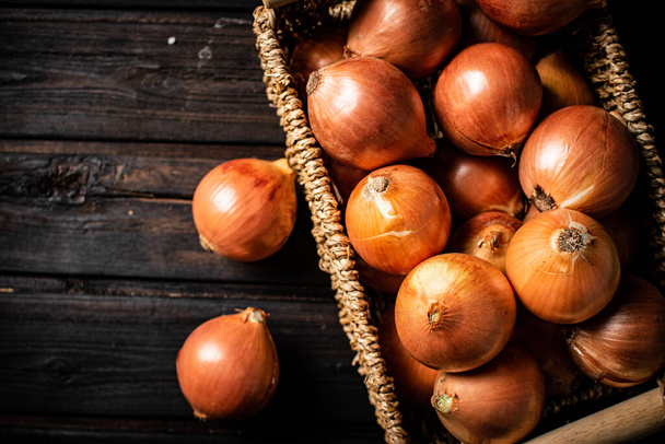 A full basket of onions on the table. On a wooden background. High quality photo - 写真・画像