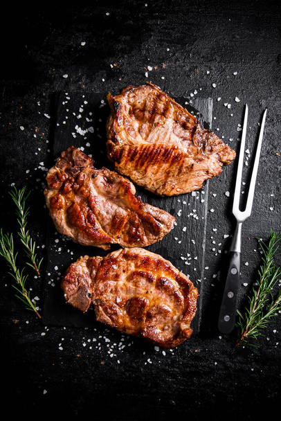 Grilled pork steak with a sprig of rosemary. On a black background. High quality photo - Foto, Imagem