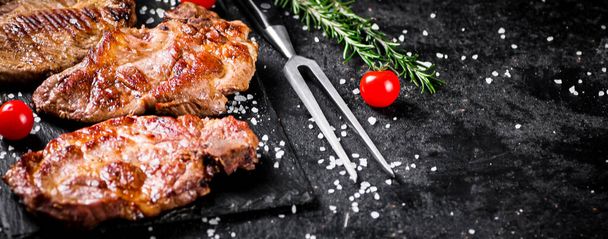 Kızarmış domuz bifteği, kiraz domatesli ve biberiyeli. Siyah bir arka planda. Yüksek kalite fotoğraf - Fotoğraf, Görsel