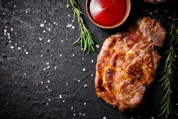 Grilled pork steak with tomato sauce and rosemary. On a black background. High quality photo - Fotoğraf, Görsel