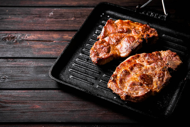 Grilled pork steak in a frying pan. On a dark wooden background. High quality photo - Φωτογραφία, εικόνα