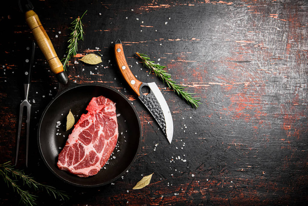 Raw pork steak in a frying pan with bay leaves and rosemary. Against a dark background. High quality photo - Φωτογραφία, εικόνα