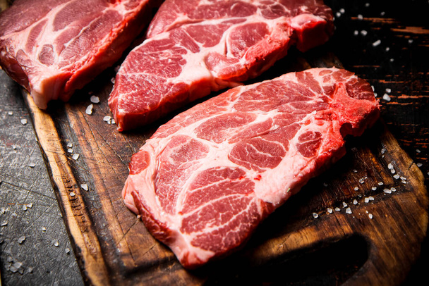 Raw pork steak on a wooden cutting board. Against a dark background. High quality photo - Foto, Imagen