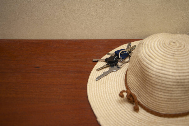 Sombrero de paja y llaves de casa sobre fondo de madera. Concepto de salir de casa, salir de casa por vacaciones, por vocación. - Foto, imagen