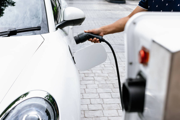 Progressive concept of hand attaches an emission-free power connector to the battery of electric vehicle at home. Electric vehicle charging via cable from charging station to EV car battery - Φωτογραφία, εικόνα