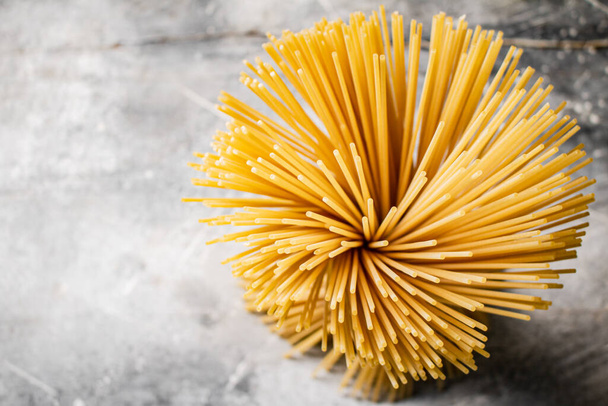 A bundle of spaghetti dry tied with a rope stands on the table. On a gray background. High quality photo - Photo, Image