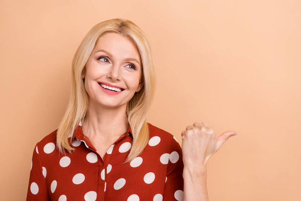 Portrait of funny toothy beaming woman with blond hair red shirt look directing at sale empty space isolated on beige color background. - Fotografie, Obrázek