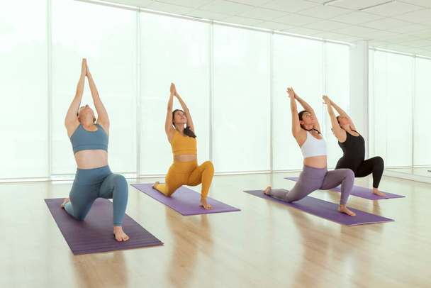Young women doing Virabhadrasana 1 pose, while practicing yoga in a studio in Mexico City - Foto, imagen