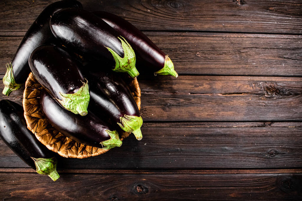 Ripe eggplant in a basket on the table. On a wooden background. High quality photo - Foto, Imagem